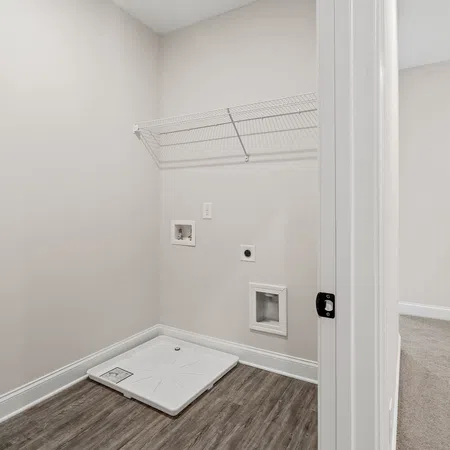 Empty laundry room with wood-look flooring, white wire shelf, and hookups for washer and dryer installation.