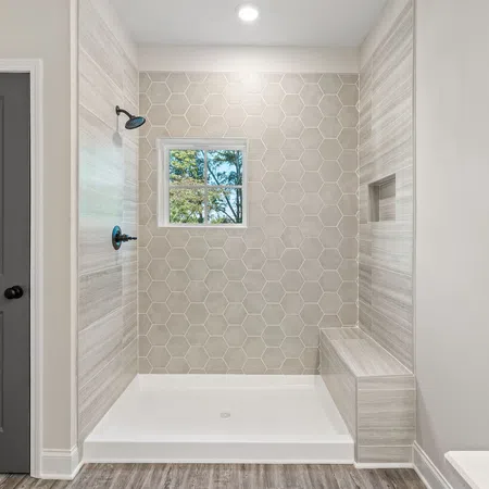 Modern bathroom shower with hexagonal tile wall, built-in bench, window, and black shower fixtures.
