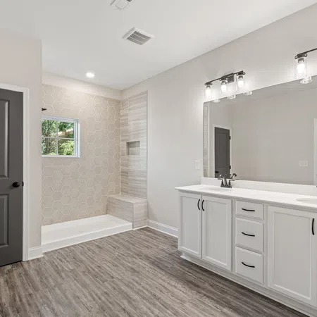 Modern bathroom with double white vanity, large mirror, walk-in shower with bench, and wood-look flooring