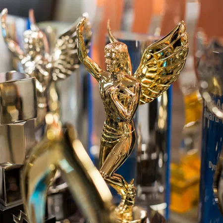 Shiny trophies with wings and awards displayed on a shelf, symbolizing achievement and recognition.