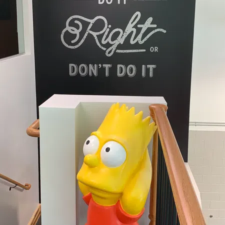A colorful Bart Simpson statue stands near a motivational wall sign saying 'Do it Right or Don't Do it.'
