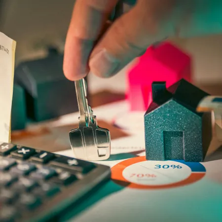 Hand holding a key over house models, calculator, cash, and pie chart representing real estate investment and mortgage finance.
