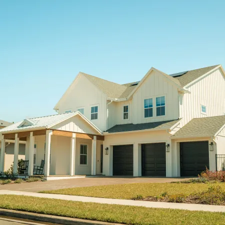 Modern two-story white house with black garage doors, front porch, and neatly landscaped lawn under clear blue sky.