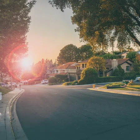 Sunset over a quiet suburban street lined with houses, trees, and parked cars on a peaceful neighborhood road.