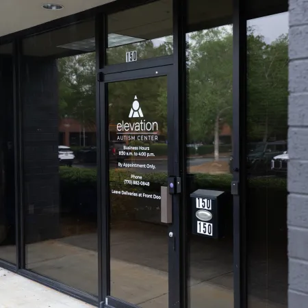 Glass entrance door to Elevation Autism Center with business hours and appointment details displayed.