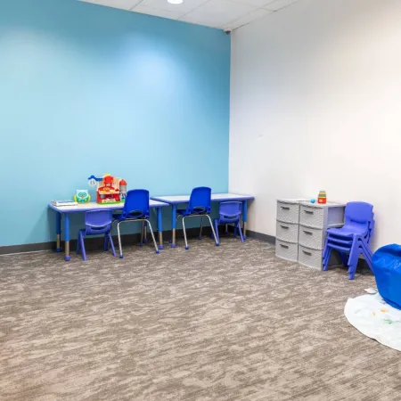 Bright and colorful children's playroom with blue chairs, tables, toys, and beanbags on carpeted floor.