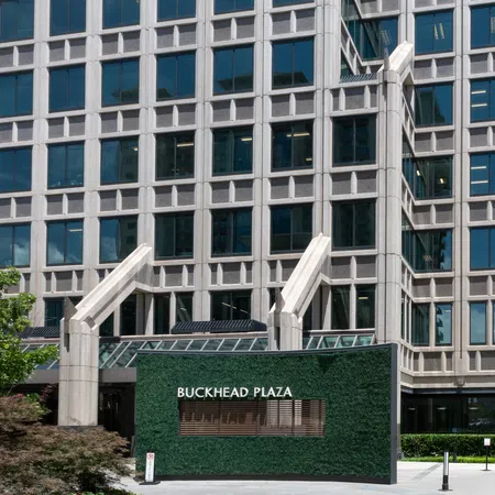 Buckhead Plaza entrance with green wall signage in front of a modern glass office building under bright daylight.