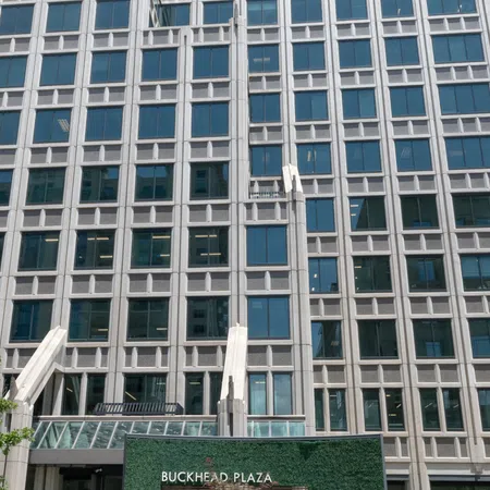 Facade of Buckhead Plaza office building with glass windows and a green sign in front.