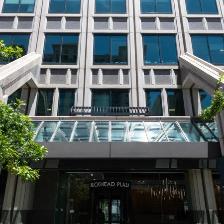 Modern office building entrance with glass doors and reflective windows at Buckhead Plaza under sunlight.
