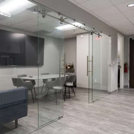 Modern office meeting room with glass sliding doors, round table, chairs, and large wall-mounted TV.