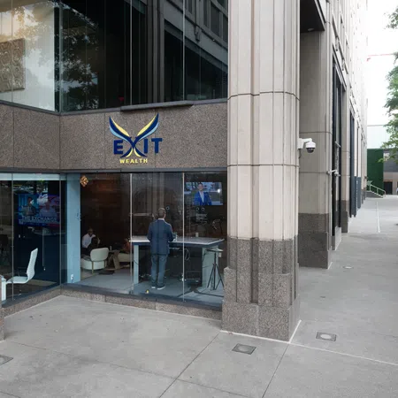 Modern office building entrance with glass walls showing people inside and EXIT Wealth logo above door.