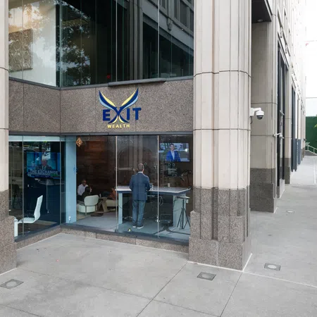 Corner office building with EXIT Wealth sign and people inside seen through large glass windows.