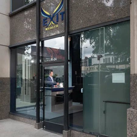 Office entrance of Exit Wealth with glass door, visible receptionist, and city reflections outside.