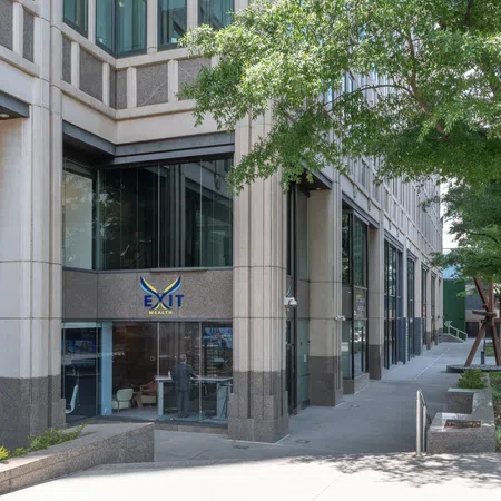 Street view of modern office building with EXIT Wealth signage and trees along the sidewalk on a sunny day