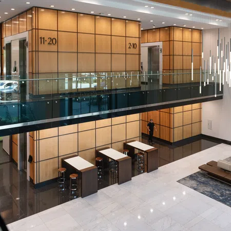 Modern office lobby with wood-paneled walls, glass railings, seating area, and contemporary light fixtures.