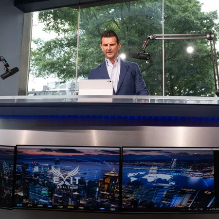 Businessman in studio presenting behind glass desk with cityscape screens and microphones in background