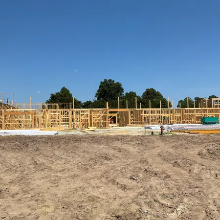 Wooden frame structure of a building under construction on clear land with blue sky and trees in the background.