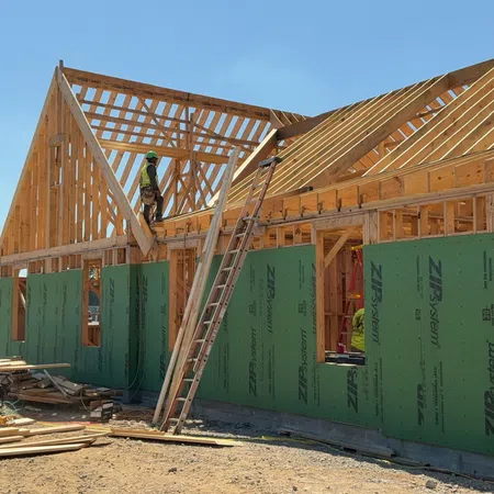 Construction workers building wooden frame and roof structure on a new residential house on a sunny day