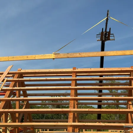 Construction workers lifting a large wooden beam onto a timber frame structure under blue sky.