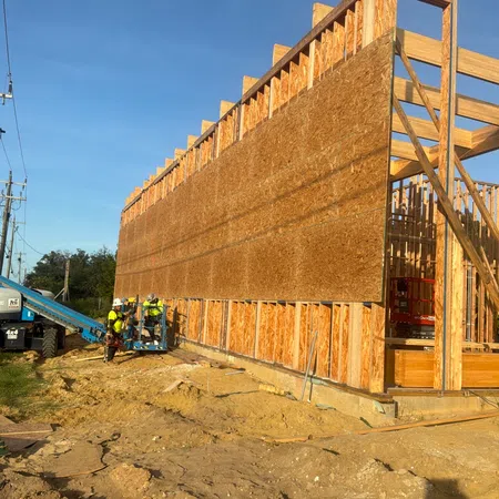 Construction workers installing large wooden panels on a building frame at a sunny construction site.