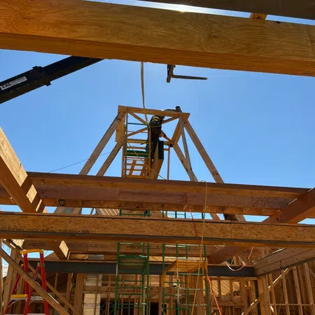 Workers assembling wooden frame structure for building construction under clear blue sky with scaffolding and ladders.