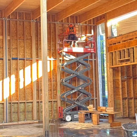 Construction worker on scissor lift inside wooden framed building under construction with sunlight streaming in
