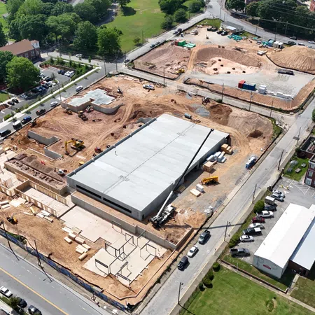 Aerial view of a construction site with partially built structures and surrounding roads and buildings in a green urban area.