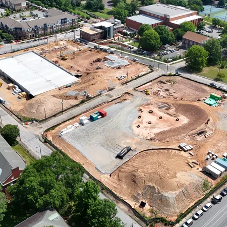 Aerial view of a large construction site with cleared land, building foundations, and heavy machinery in a suburban area.