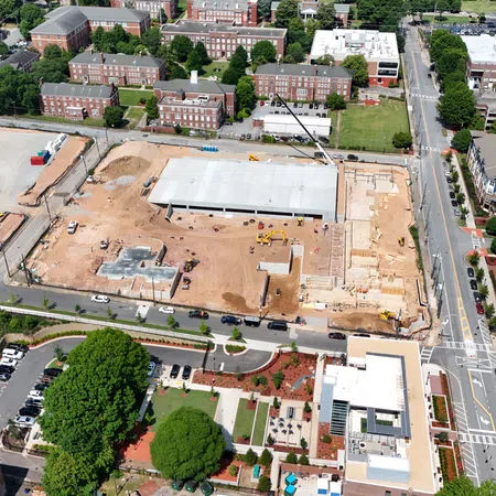 Aerial view of urban construction site with buildings, roads, parking lots, and trees in a residential neighborhood.