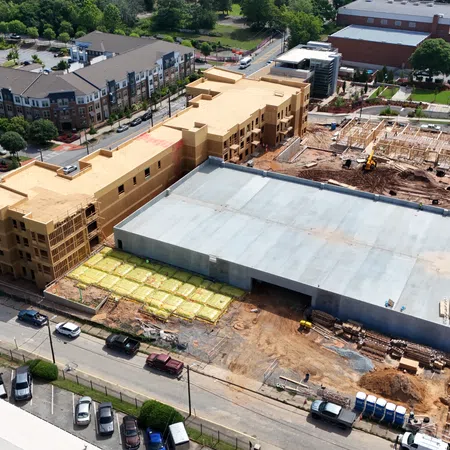 Aerial view of a large mixed-use building under construction with surrounding residential and commercial areas.