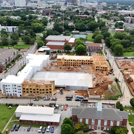 Aerial view of a mixed-use construction site with residential buildings, green spaces, and city skyline in the background.