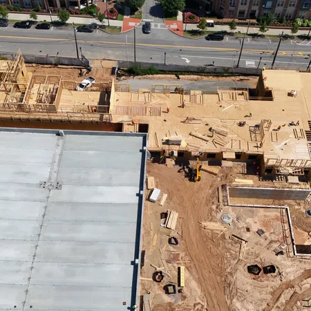 Aerial view of a construction site with wooden framing and a large concrete structure near a busy street.