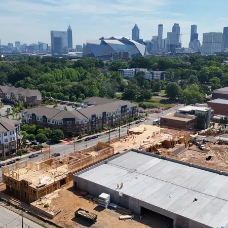 Aerial view of urban construction site with residential buildings and city skyline in the background under clear sky.