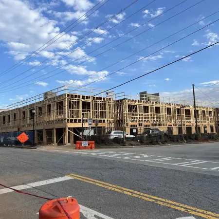 Wooden framework of a multi-story building under construction on a clear day with traffic cones and street signs.