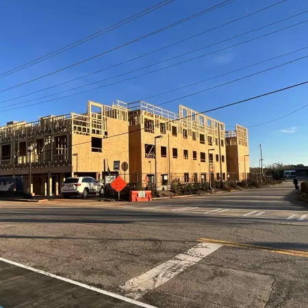 Wood-framed multi-story building under construction near a street with clear blue sky and power lines overhead