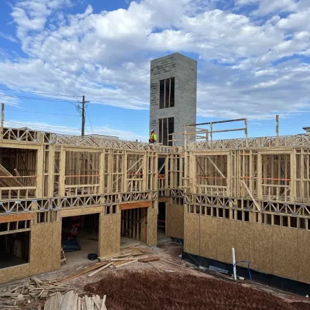 Wooden framework of a multi-story building under construction with a worker and blue sky with clouds.
