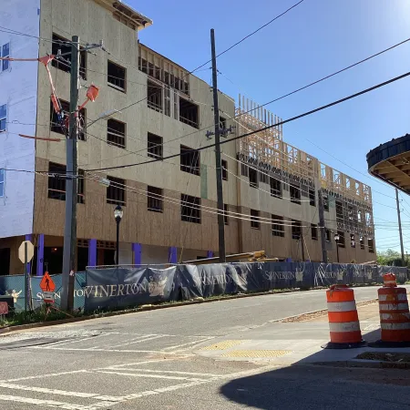 Mid-rise building under construction with wooden framework and protective fencing on sunny day.