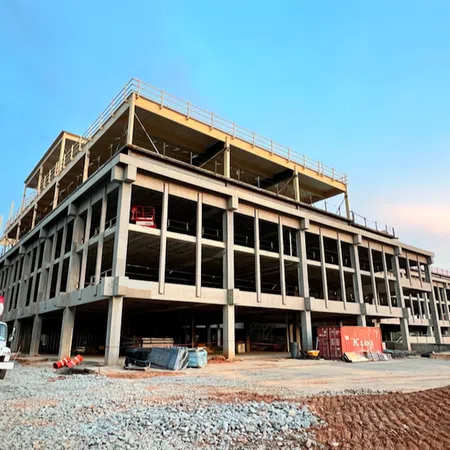 Multi-story commercial building under construction with concrete framework and construction vehicles on site under clear sky