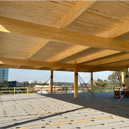 Under-construction building with wooden beams and columns supporting the ceiling with cityscape in background.