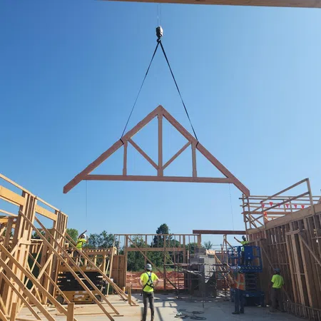 Construction workers installing a wooden roof truss on a building frame under clear blue sky.