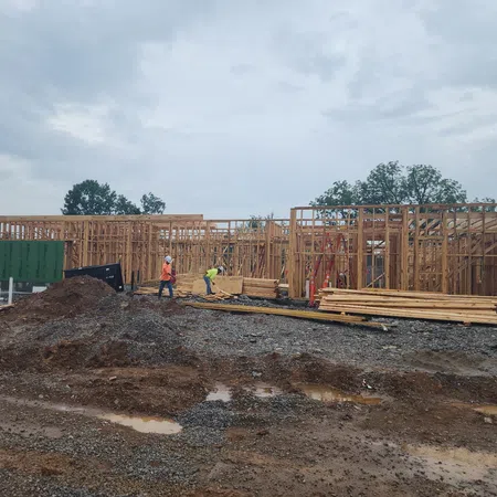 Workers building wooden frame structure of a house at a muddy construction site on a cloudy day.