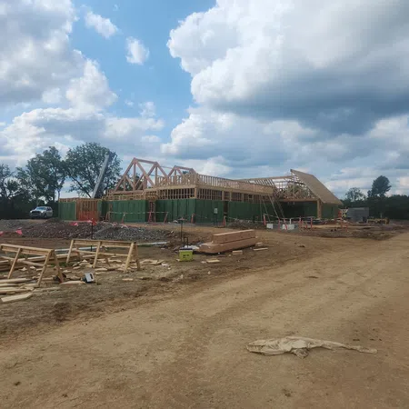 Construction site with wooden framework building under a cloudy sky on a dirt road with scattered materials.