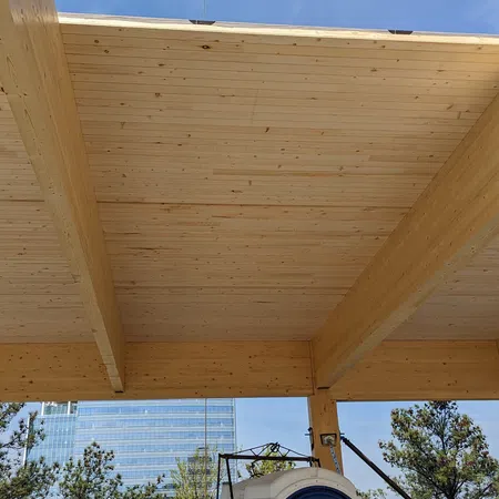 Wooden beams and ceiling under construction with a portable toilet and cityscape in the background on a clear day