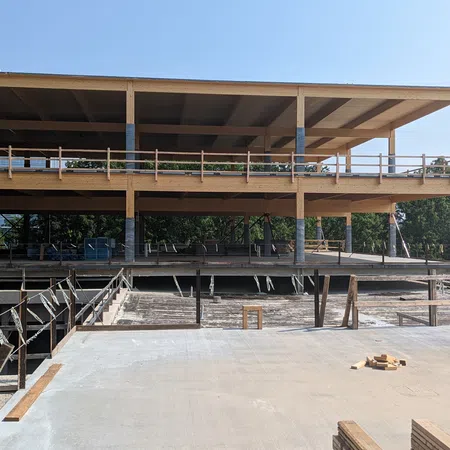 Wooden multi-level building under construction with clear blue sky and concrete ground in foreground.