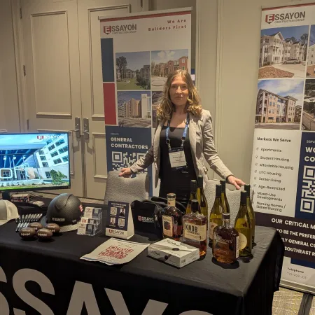 Woman standing at Essayon Construction booth with promotional items and banners at a trade show or conference.