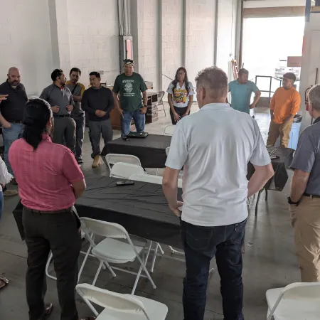Group of diverse people standing in a circle inside a warehouse during a team meeting or discussion.