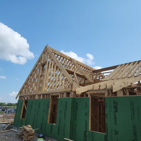 Wooden frame and green sheathing panels on a house under construction against a blue sky.