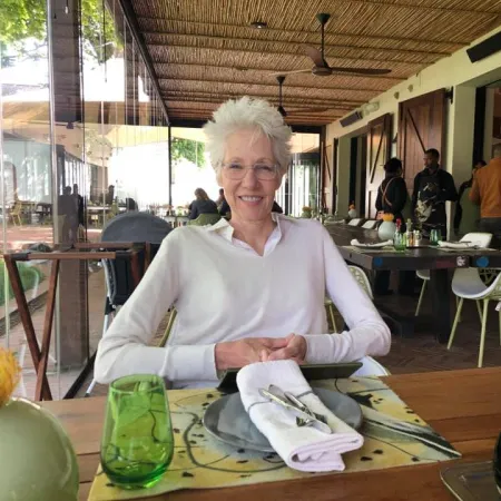 Smiling elderly woman sitting at a table in a bright, modern restaurant with wooden accents and glass walls.