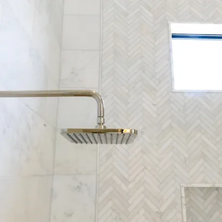 Modern silver showerhead mounted on tiled wall with a window above.