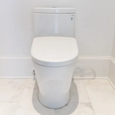 Modern white toilet in a clean bathroom with marble flooring and minimalistic decor.